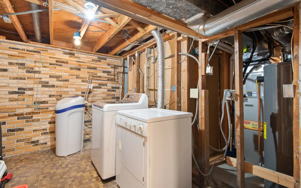 Basement utility area with a gas water heater standing beside a furnace, a water softener, and a washer and dryer under open floor joists