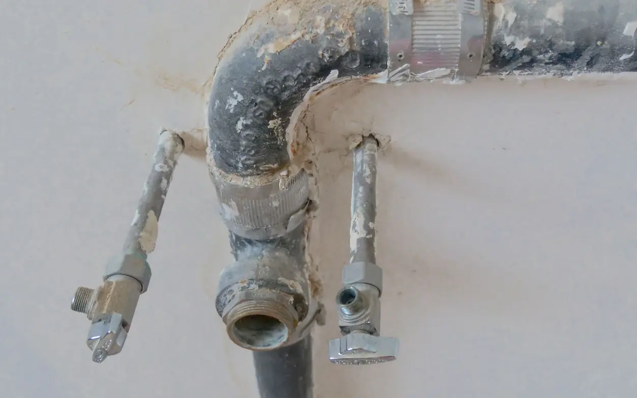 Galvanized water line opened up inside a wall, showing a threaded capped stub and two chrome quarter-turn shutoff valves